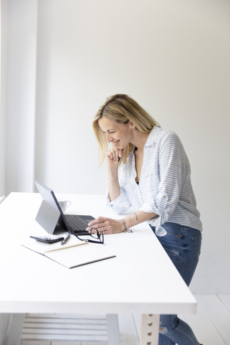 pretty young business woman standing by her desk and working on tablet from home in her home office